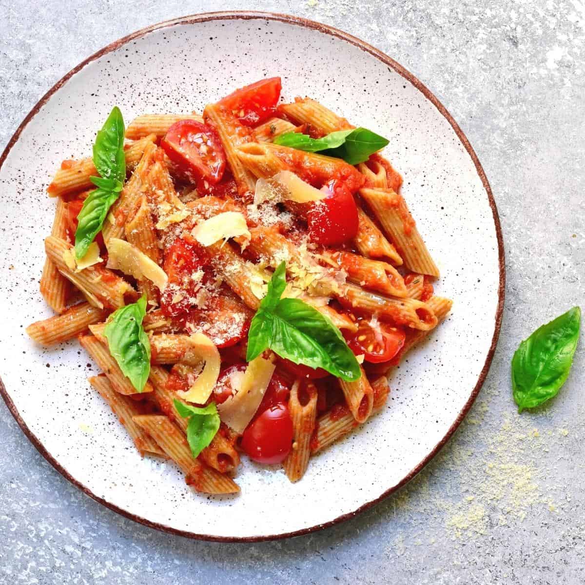 A white ceramic plate with pink sauce pasta topped with fresh basil leaves.