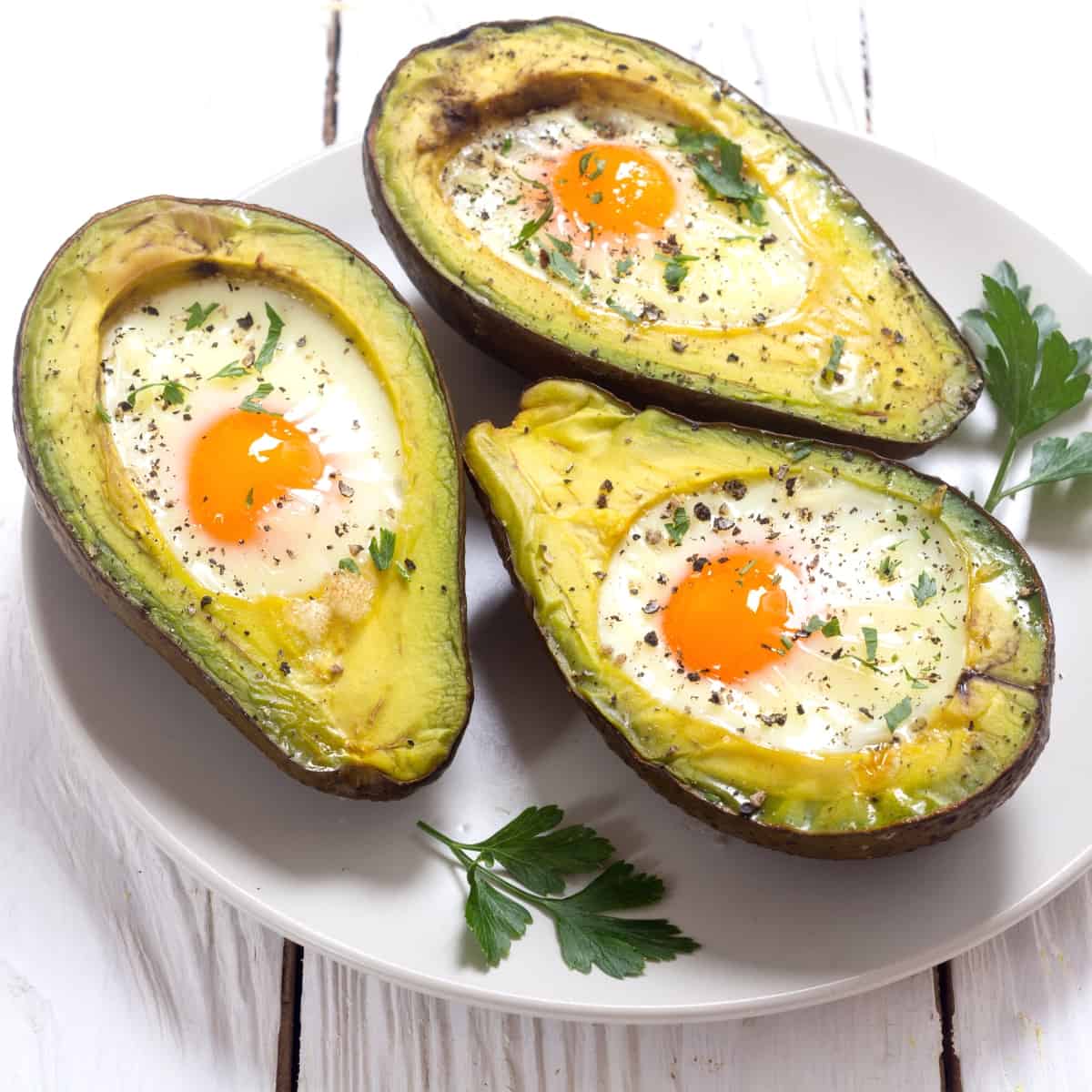 A white plate topped with baked eggs in avocados.