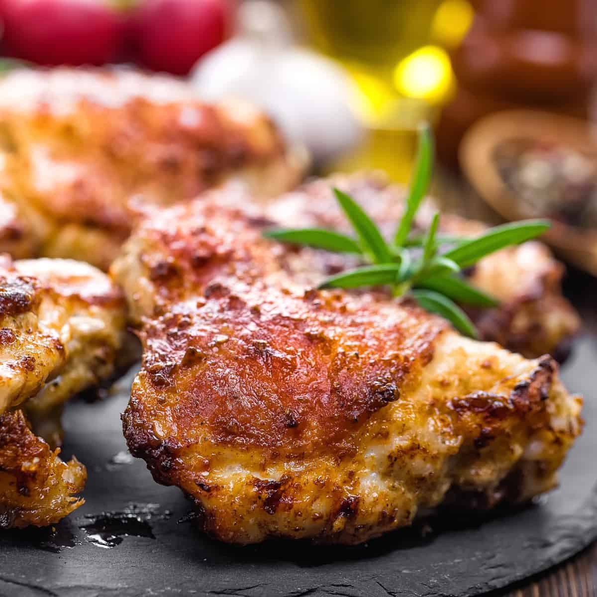 Chicken thighs on a black plate topped with fresh green herbs.