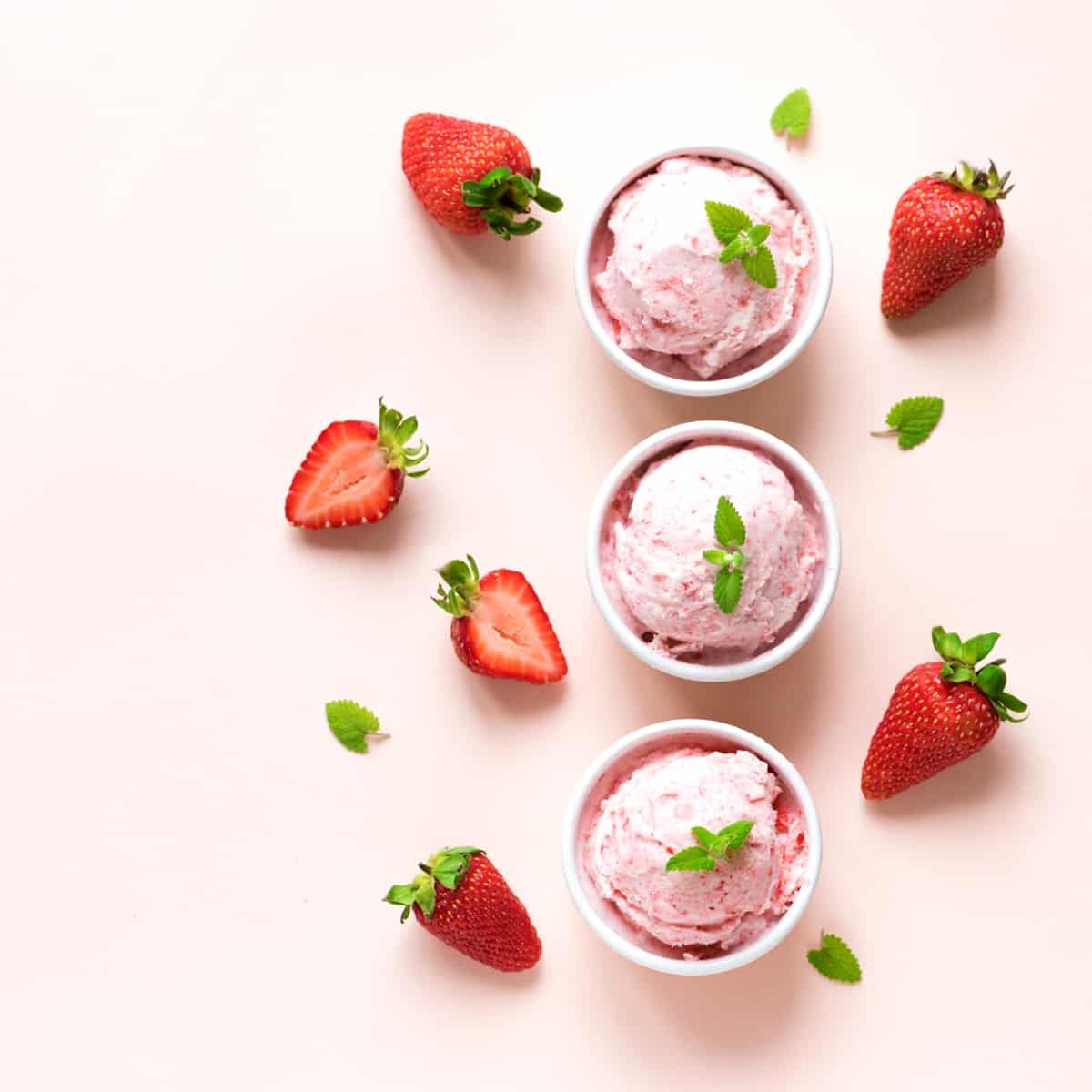 White bowls filled with pink ice cream surrounded by fresh strawberries.