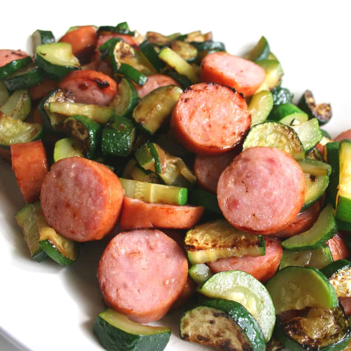 A white plate with sliced kielbasa and veggies.