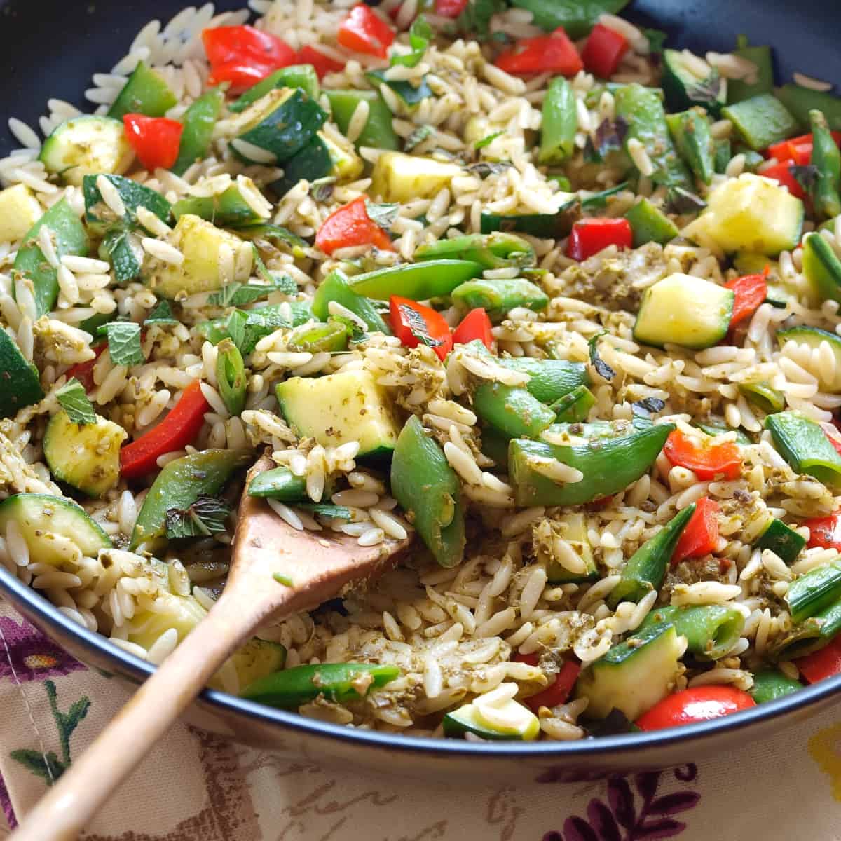 A skillet filled with orzo pasta and chopped vegetables.