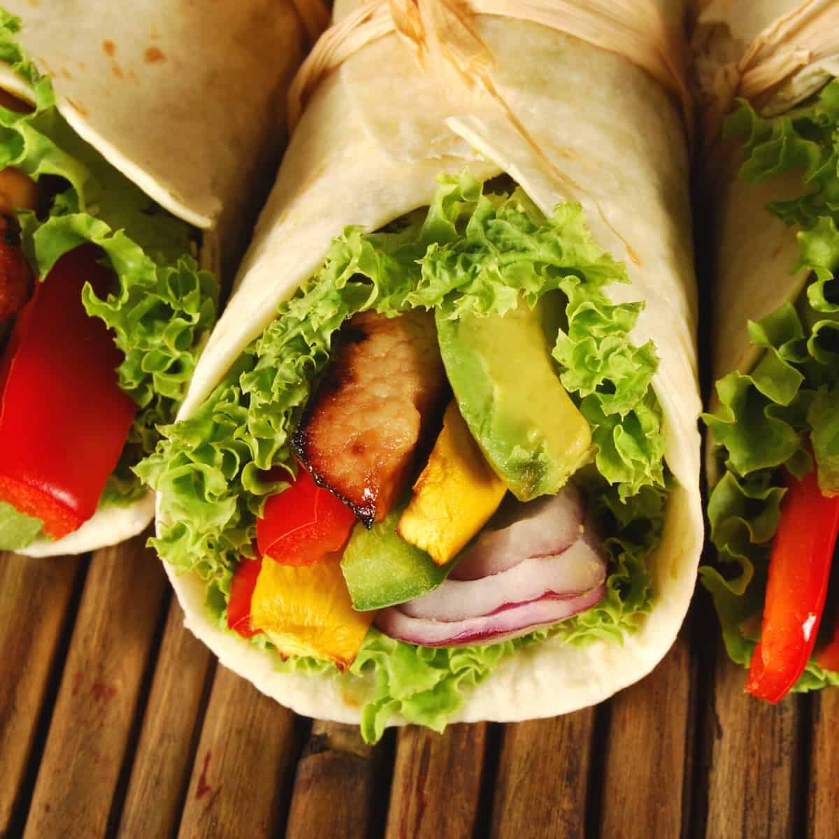 Three lunch wraps on a wooden table.