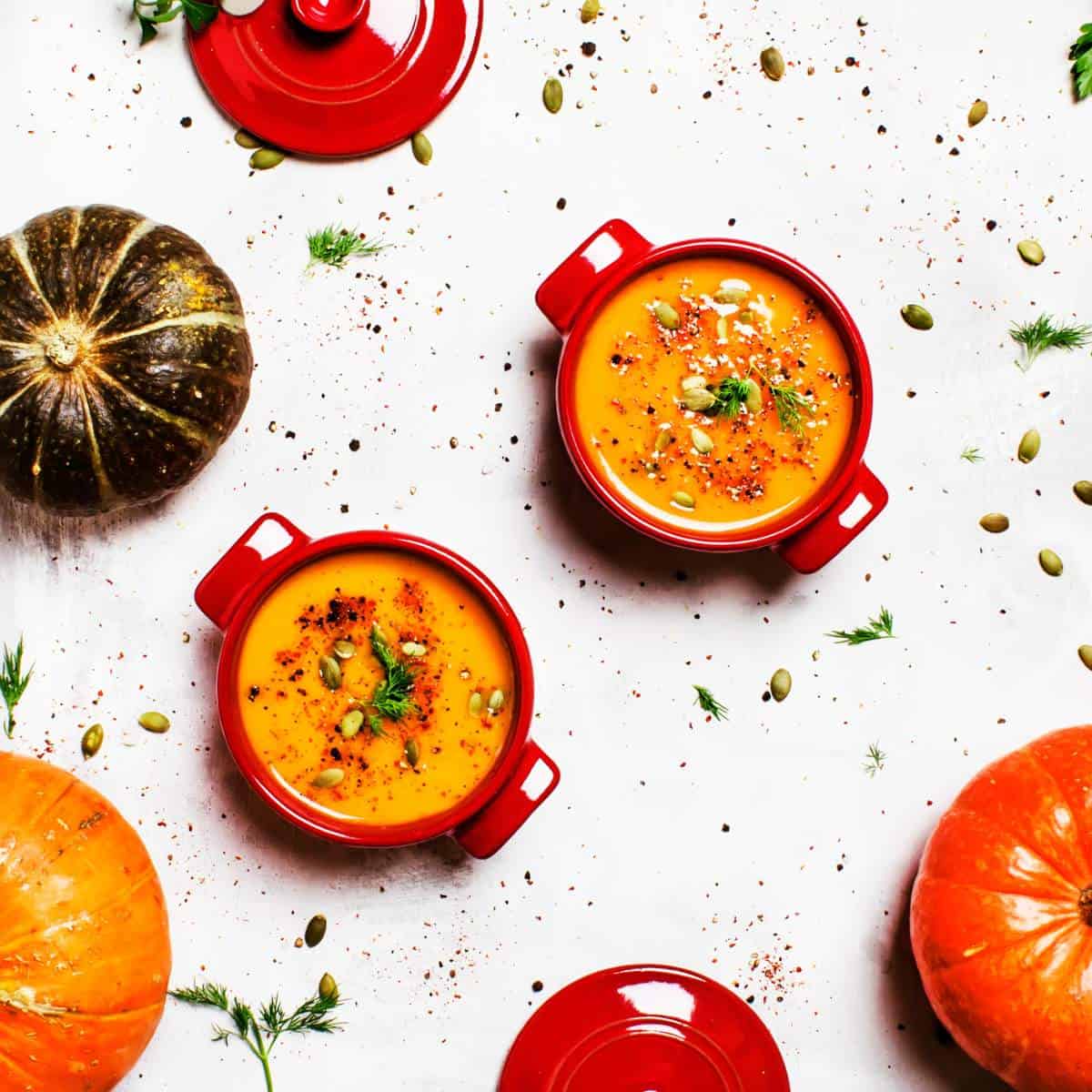 Two bowls of spicy pumpkin soup surrounded by pumpkins.