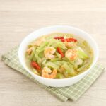 A chayote and vegetable soup on a wooden table.