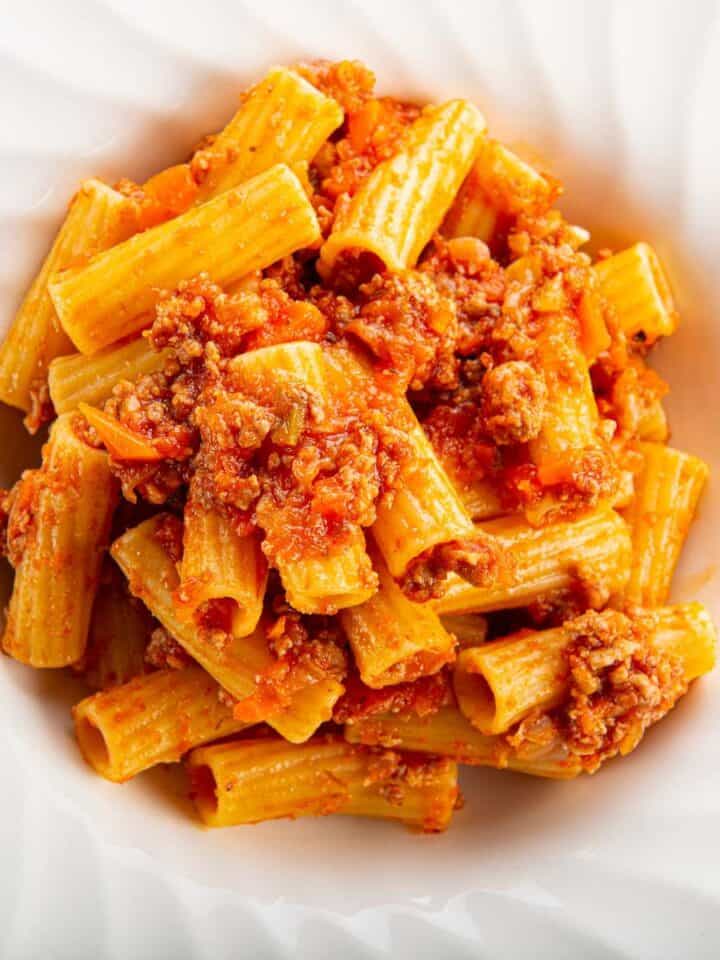 Penne pasta with ground veal meat sauce on a white plate.