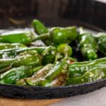 Spanish appetizers: Jalapeños sizzling in a skillet on a rustic wooden table.