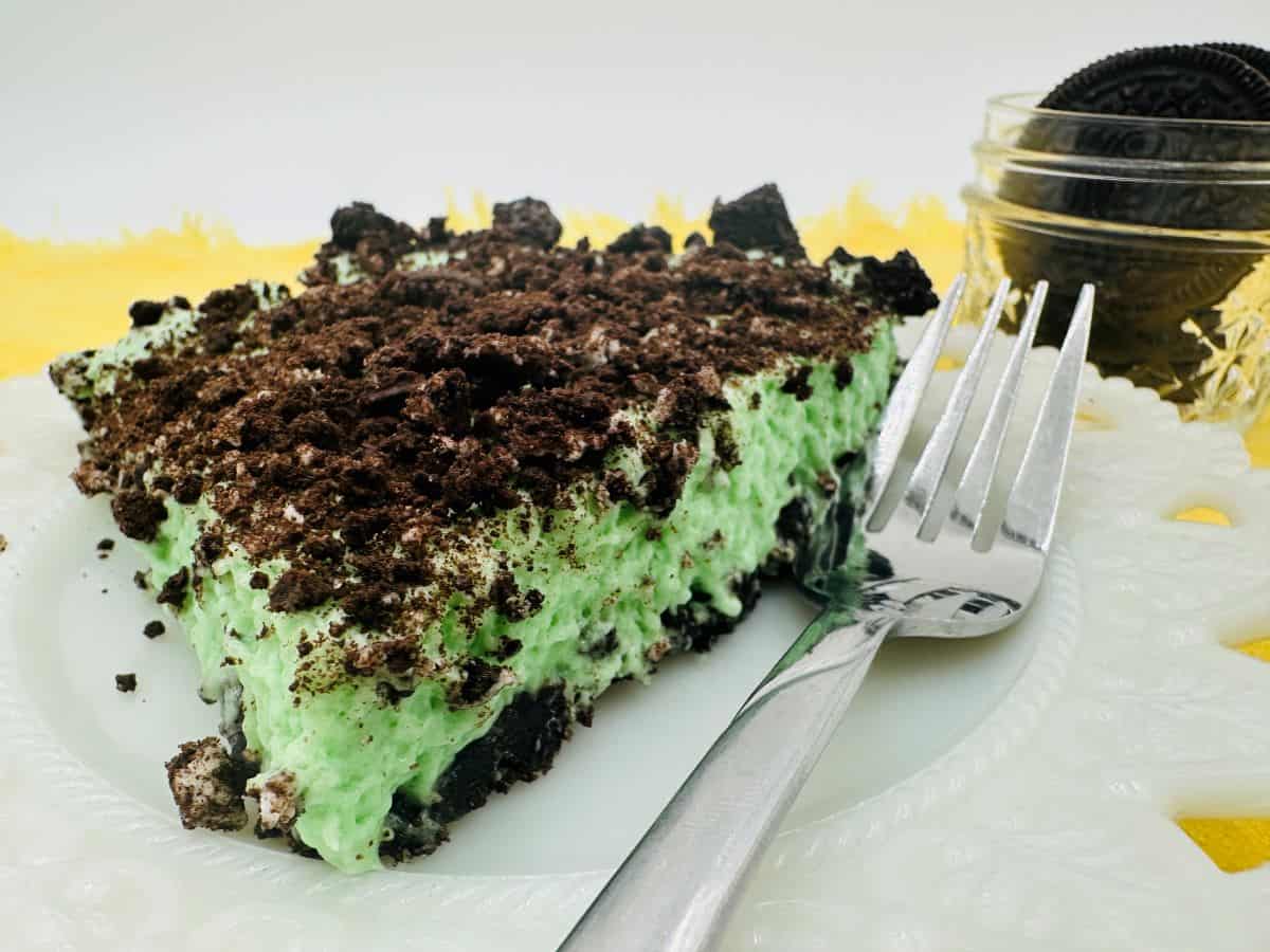 A slice of green oreo pie on a plate with a fork.