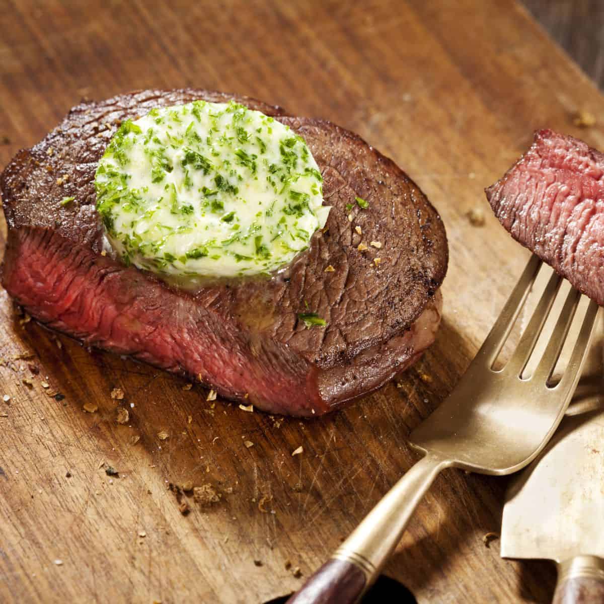 A mouthwatering steak on a cutting board with a knife and fork, ready to be enjoyed with exquisite toppings.