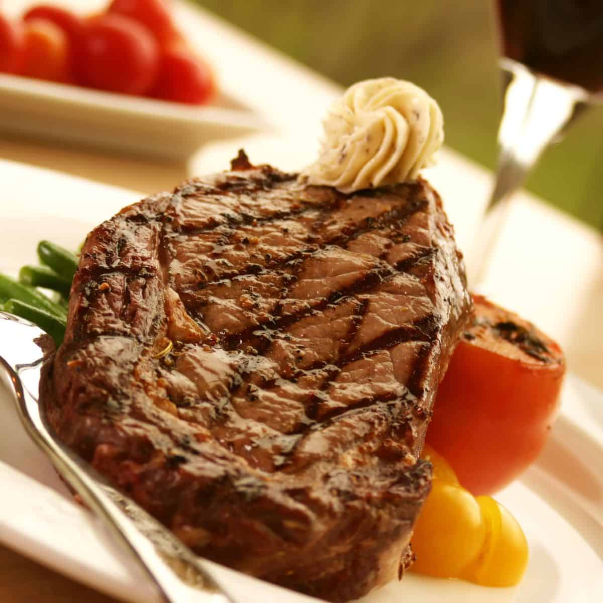 A delicious steak topped with flavorful ingredients, on a plate next to a glass of wine.