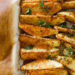 Seasoned potato wedges on parchment paper with scattered herbs.