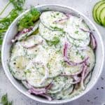 A bowl of creamy cucumber salad garnished with dill and red onion slices.