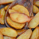 Caramelized apples in a pan with a wooden spoon.