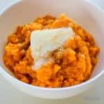 A bowl of mashed sweet potatoes topped with a melting pat of butter.