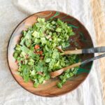 A fresh garden salad with leafy greens and chopped vegetables in a wooden bowl with salad servers.