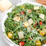 A fresh arugula salad with cherry tomatoes, cheese, and nuts served in a white bowl.