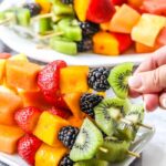 Colorful fruit skewers with a variety of fresh fruits, including strawberries, blackberries, kiwi, and melon, arranged on a white plate.