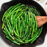 Sautéed green beans in a cast iron skillet with a wooden spoon.