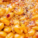 Close-up of a spoon scooping baked beans seasoned with spices.