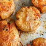 Golden-brown smashed potatoes seasoned with spices on a baking sheet.