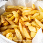 Golden french fries in a white bowl lined with a paper towel.