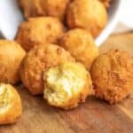 Golden brown hushpuppies on a wooden surface, with one split open to show the soft interior.