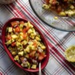 Fresh vegetable salad served in a red dish on a table with a patterned tablecloth.