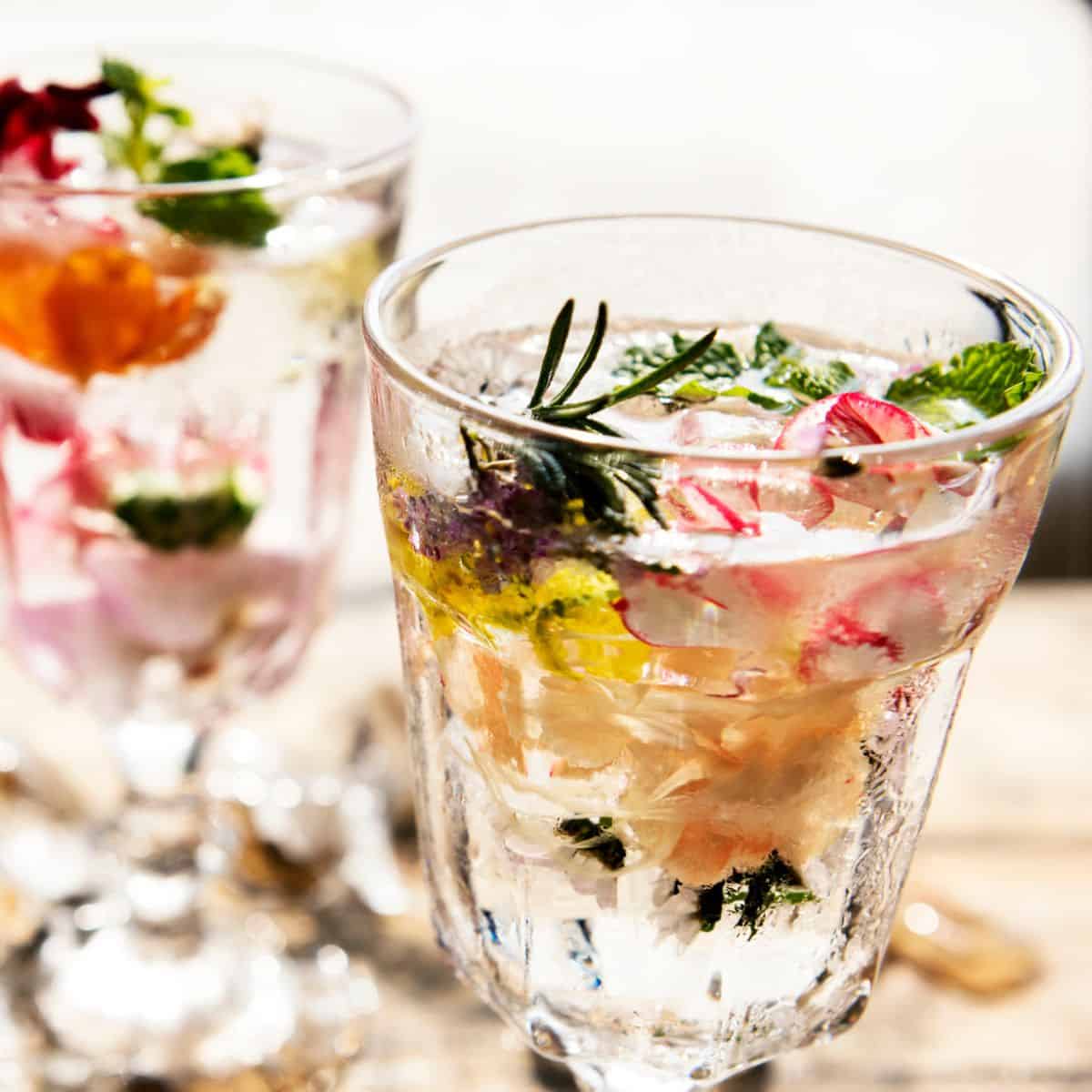 Two glasses of non-alcoholic sparkling water infused with herbs and edible flowers.