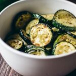 A bowl of roasted zucchini slices on a wooden table.