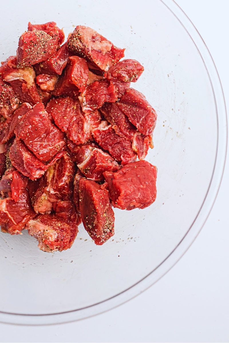 Air fryer steak bites seasoned with spices in a clear glass bowl on a white surface.