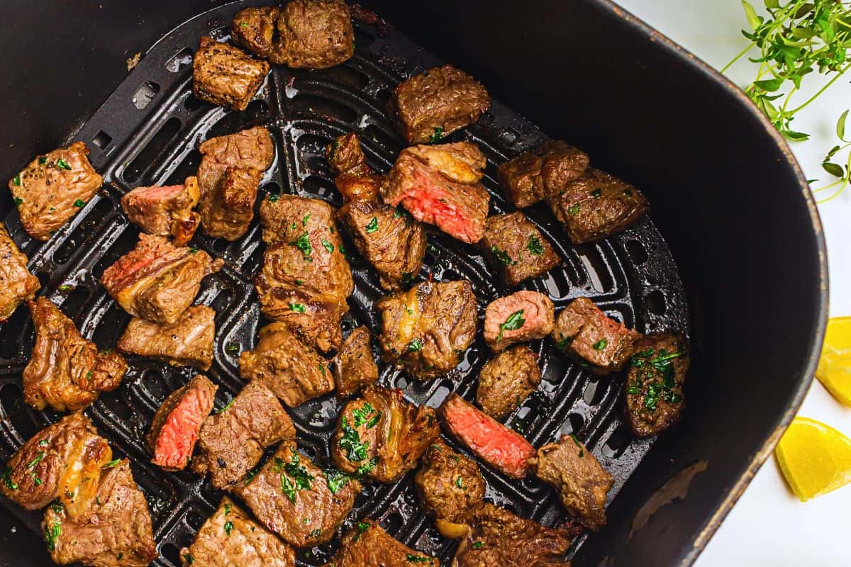 Air fryer steak bites cooking in a grill pan, garnished with herbs, showing varying degrees of doneness.