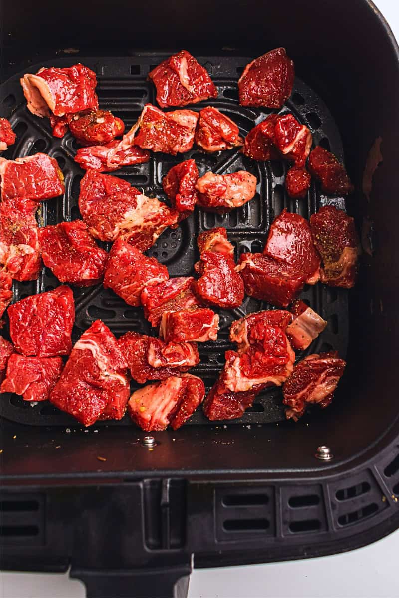 Raw, seasoned steak bites in an air fryer basket ready for cooking.