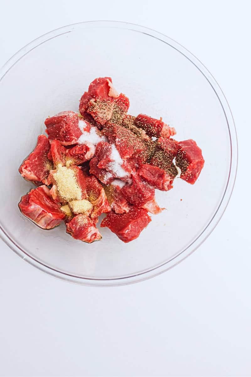 Air fryer steak bites seasoned with salt and pepper in a glass bowl on a white background.